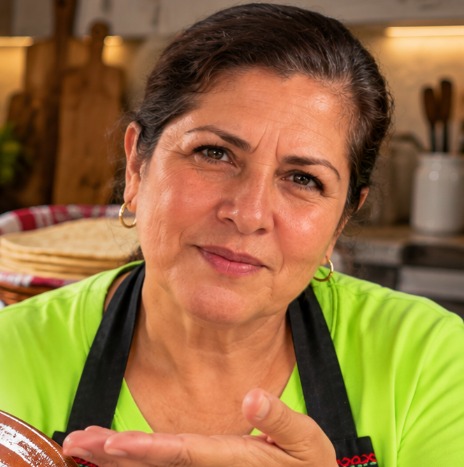 Teresa, con camisa verde y delantal, sonriendo en su cocina